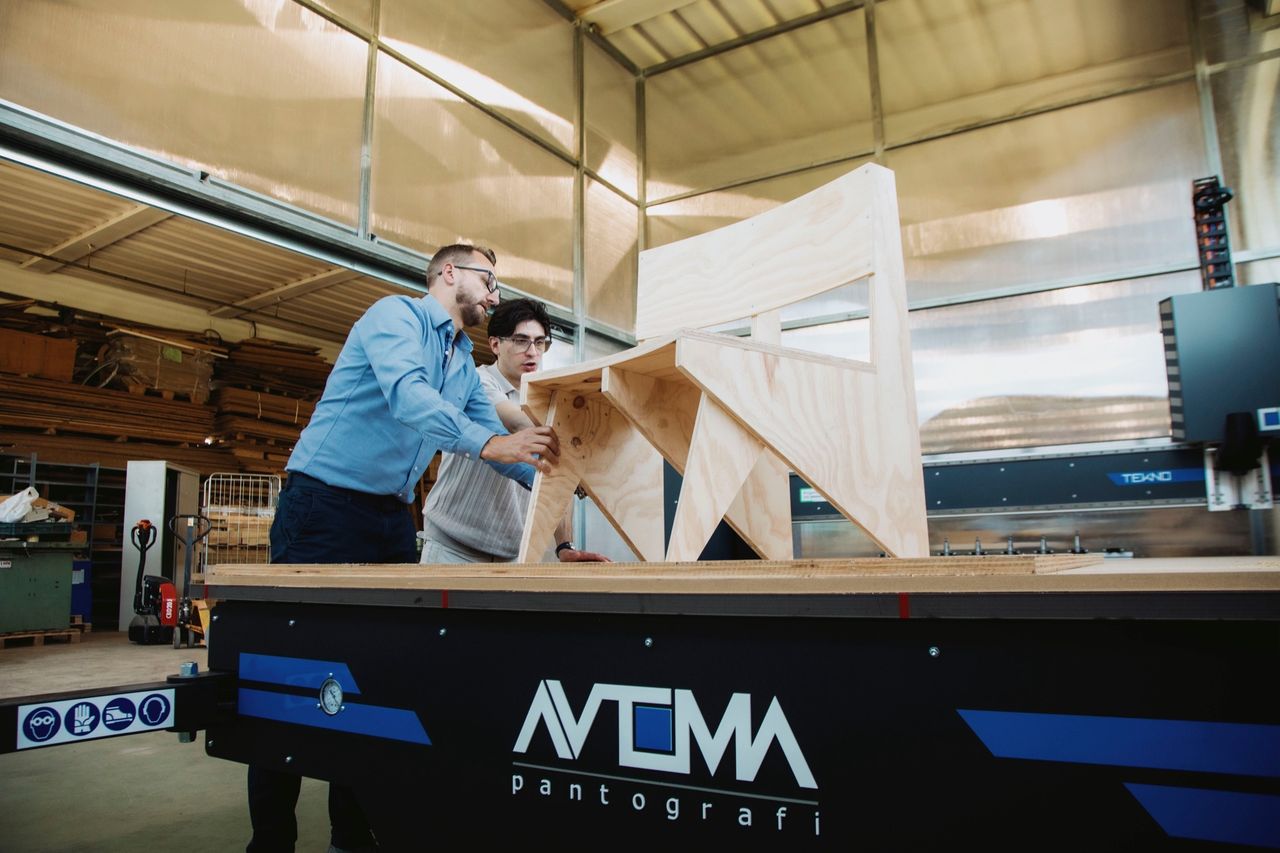 Angelo Cava solleva una sedia di legno fresata sulla TEKNO